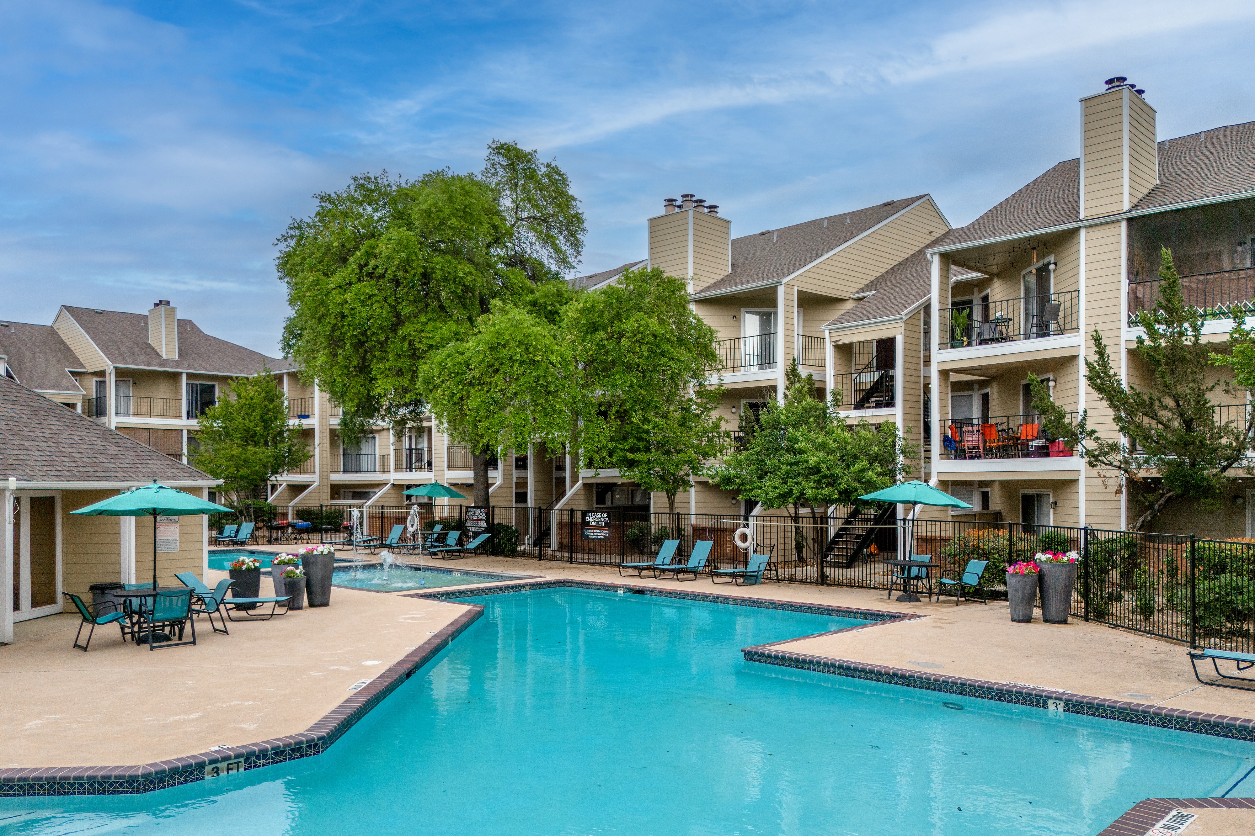 A swimming pool surrounded by lounge chairs and umbrellas in front of apartment buildings.